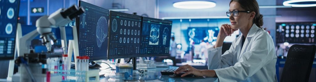 Woman in white lab coat looking at computer screens